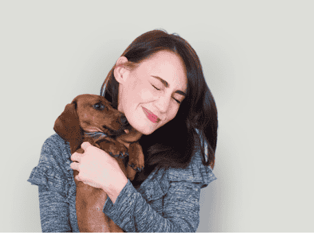 Smiling young woman hugging a brown dachshund puppy with affection, against a plain background